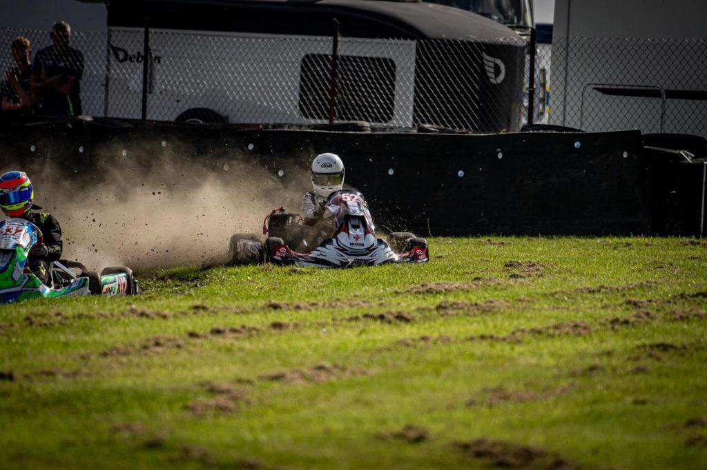 image of james kell motorsport racing at three sisters circuit in his white xkart arai helmet and sliding across the grass after a racing crash with another driver