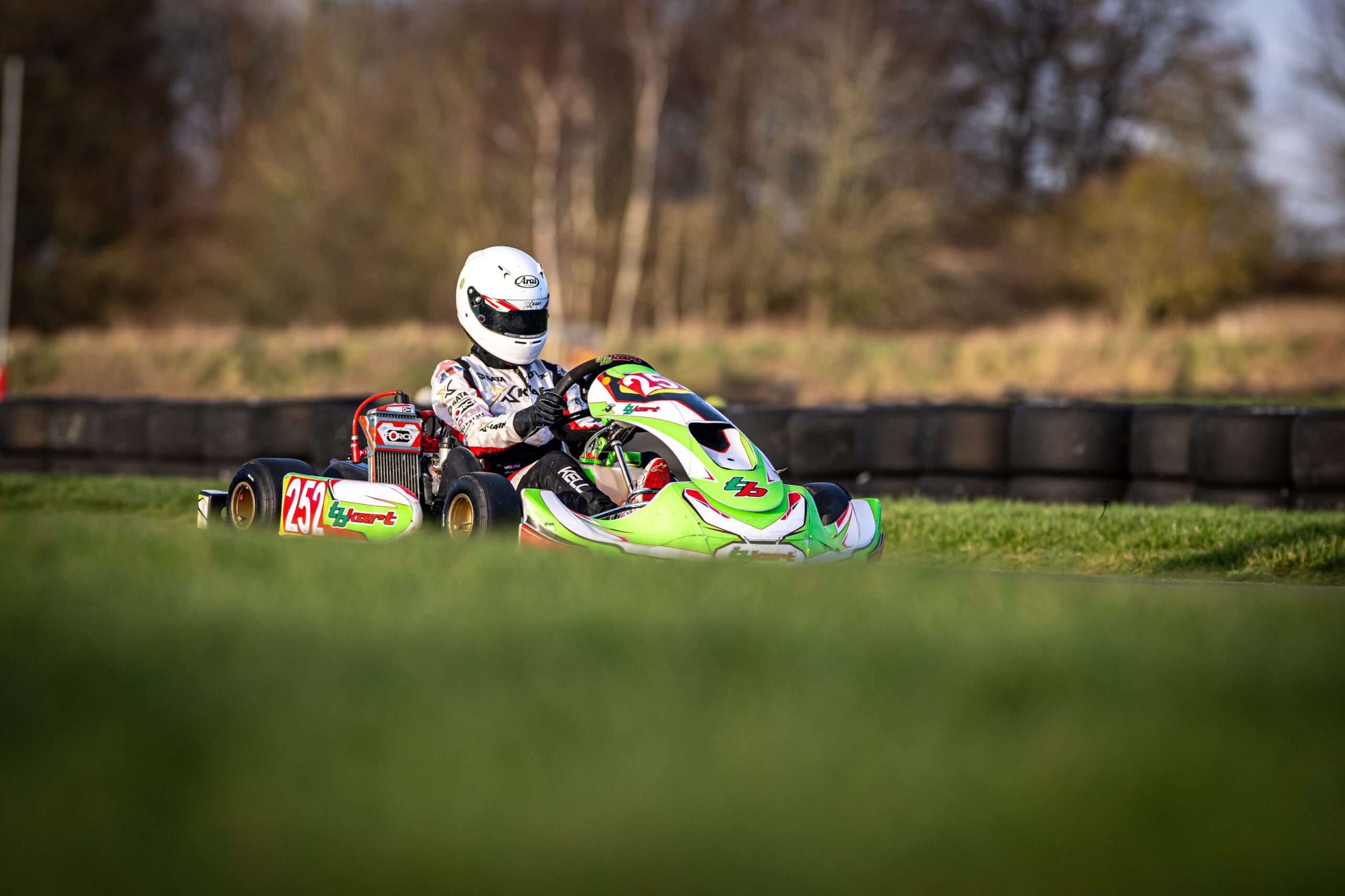 green TB kart young diver with white arai helmet grass and trees sky